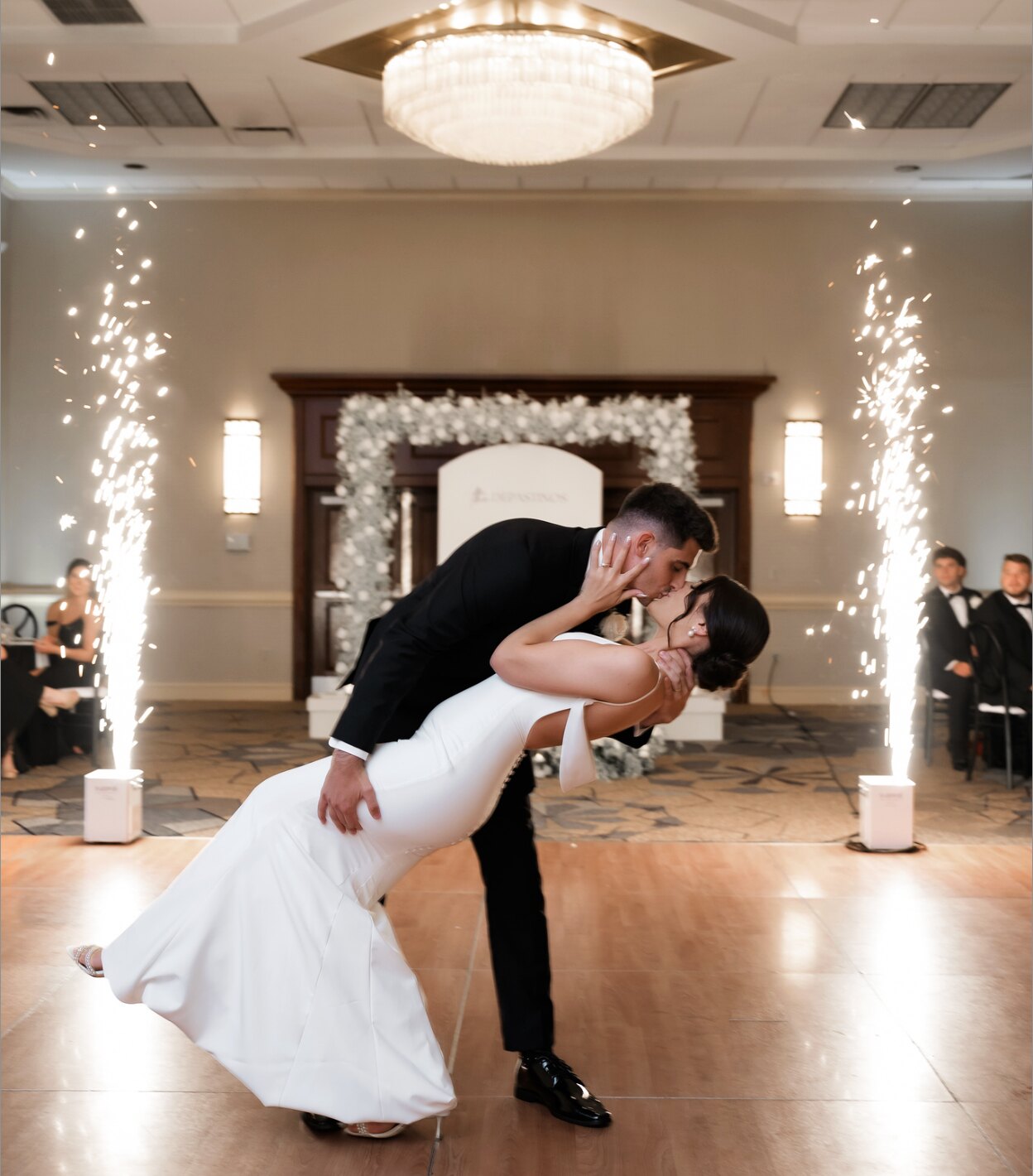 Groom dipping bride for a kiss between two columns of sparklers in a ballroom