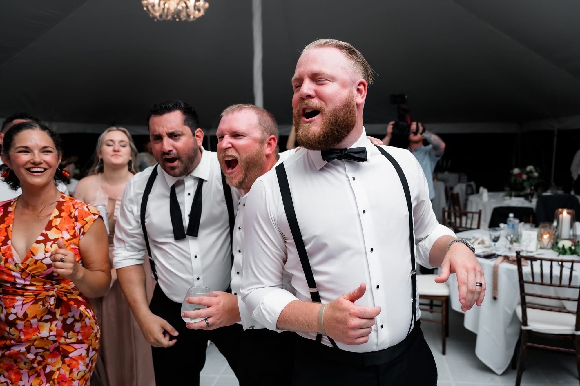 Groomsmen leaning in together to sing into the microphone at a tented private-residence reception