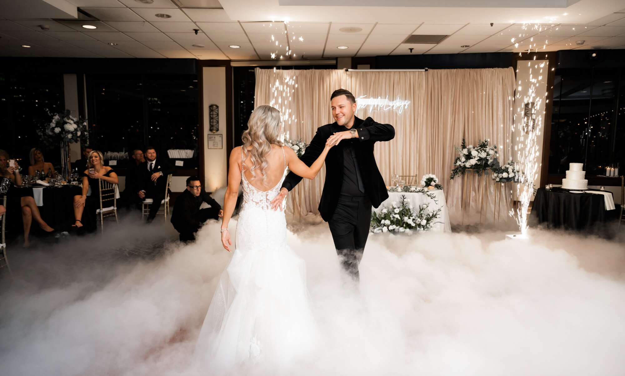 Bride and groom first dance on a fog-covered floor framed by indoor sparklers